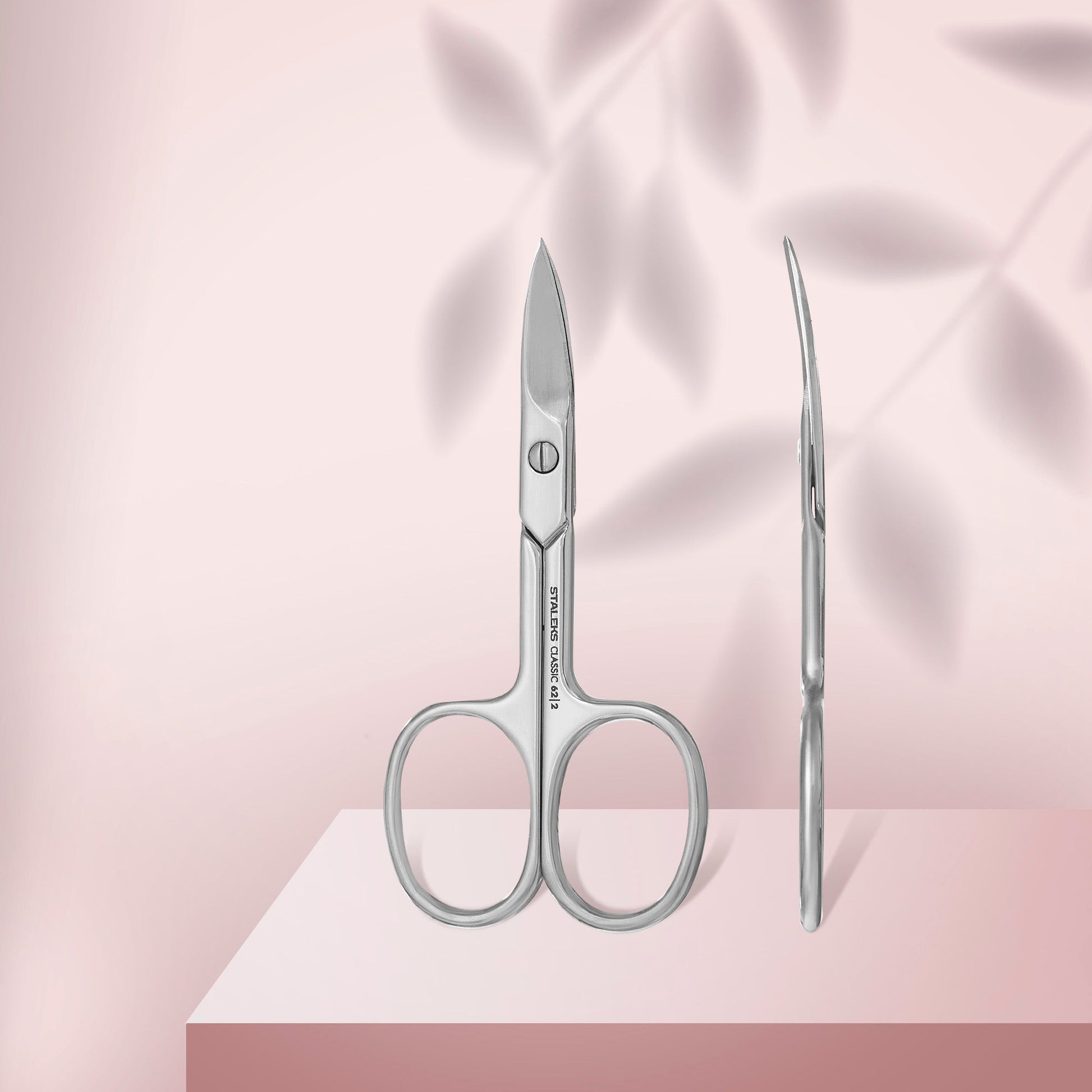 Pair of scissors and a needle on a pink fabric background