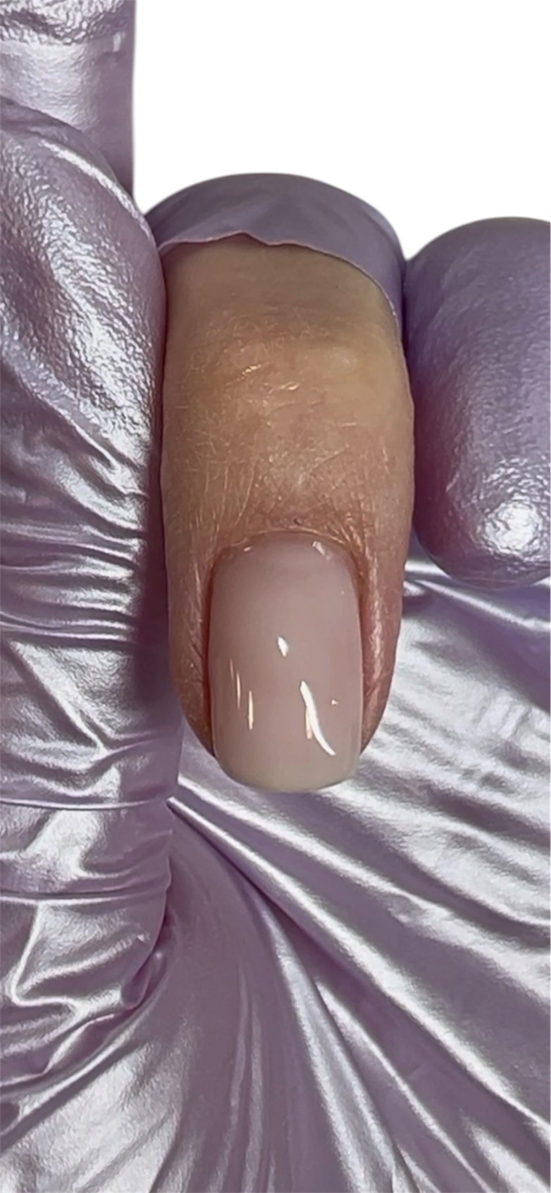 Close-up of a beige nail with a white base coat on a textured white background